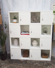 White metal industrial locker-style shelf with decorative items against a white wall.