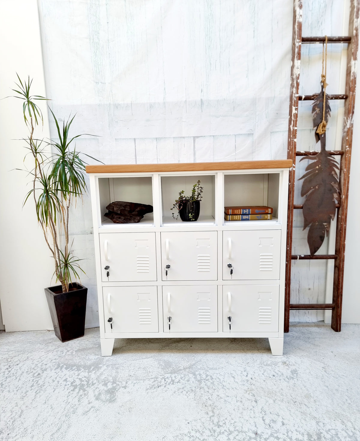 A white 9-door locker with rimu top, featuring white handles and a lock mechanism on each door, positioned against a white background with a potted plant to the side.