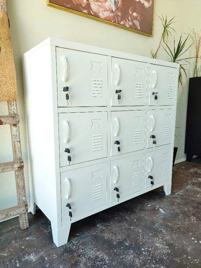 A white metal 9-door locker with each door featuring lockable hidden storage. In a showroom.
