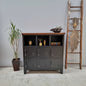 A black 9-door metal locker with a dark Rimu top, situated against a wall with a ladder and a potted plant beside it. The locker has a industrial style with visible handles and a textured finish.