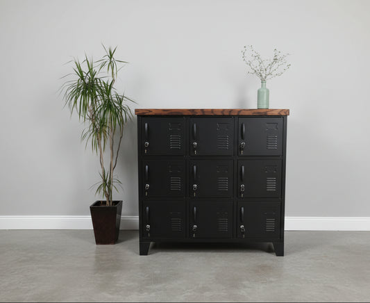 Black metal 9-door locker with dark oak top, featuring a potted plant to the left and a ladder in the background.