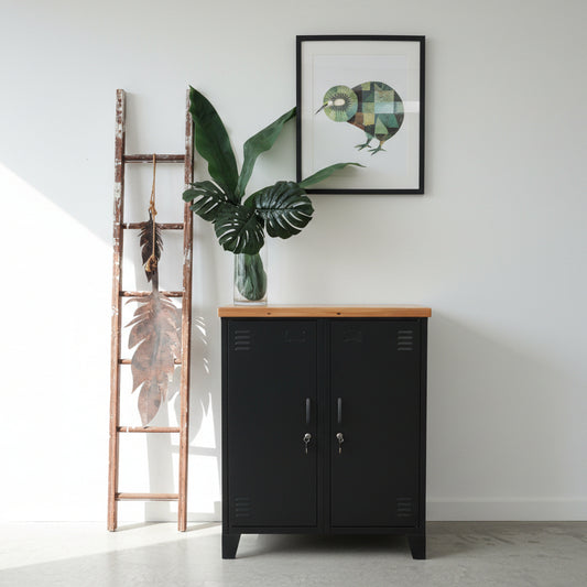 Black double side cabinet with a recycled Rimu top, featuring two adjustable shelves, placed on a white floor with a large plant to the side and a wooden ladder in the background.