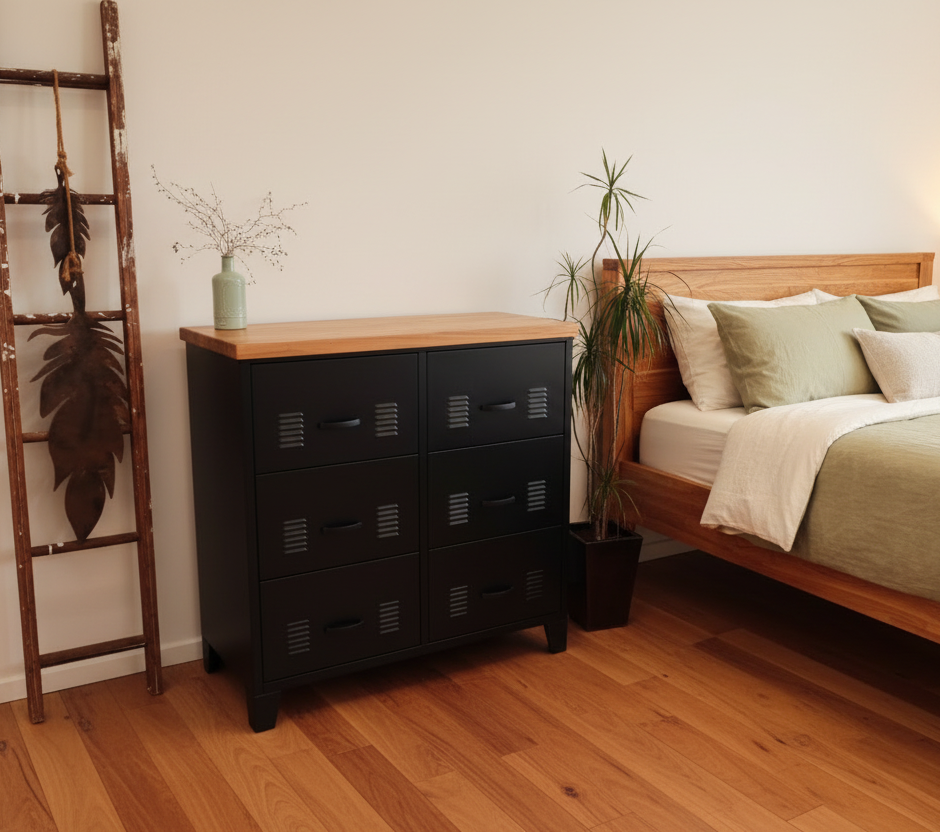 Black metal 6 drawer tallboy with Rimu top in a room with a white textured wall, plant, and decorative ladder.