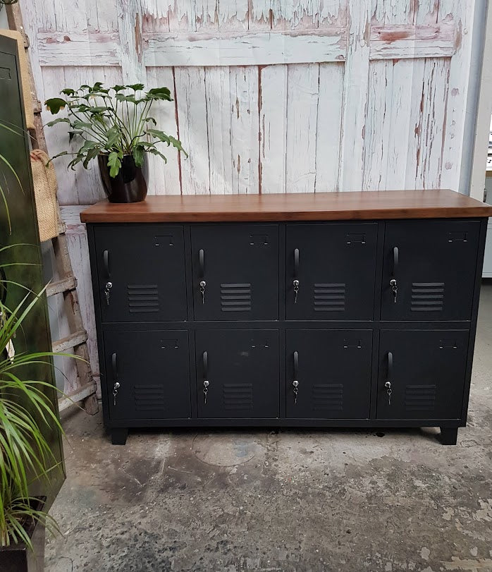 Black metal 8 door locker cabinet with a Dark Rimu wooden top against a rustic wooden wall.