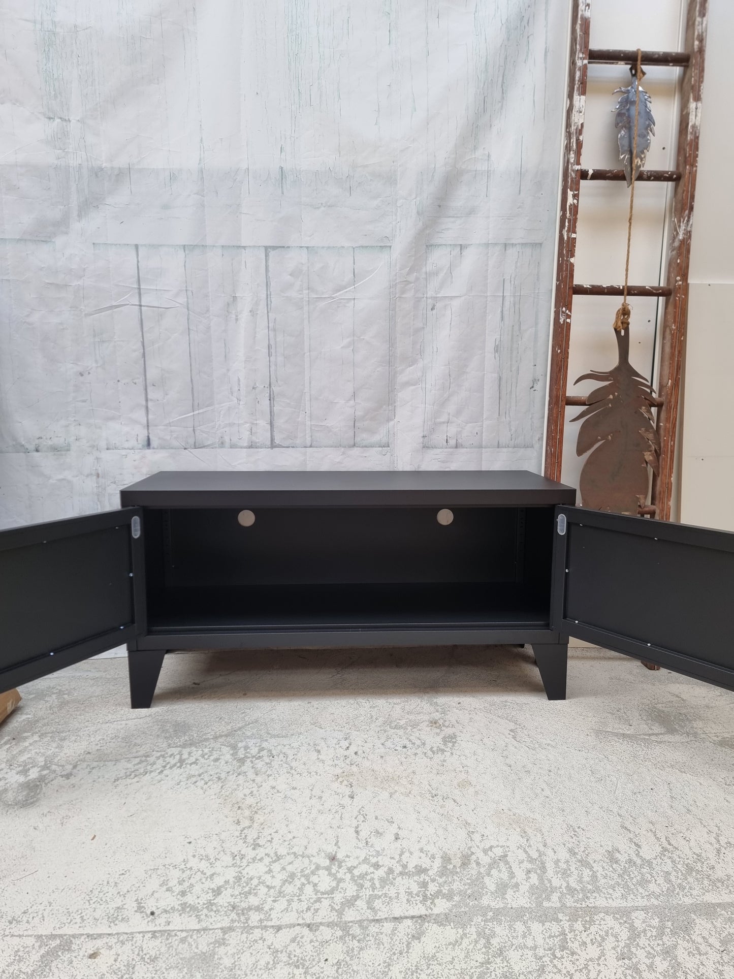 Black metal TV cabinet with open doors showing inside with cable holes