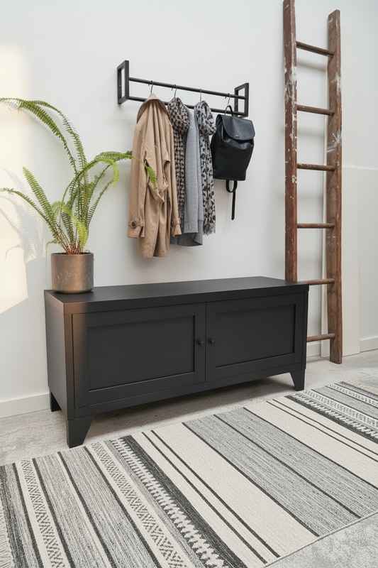 Black metal bench with coat rack against a white wall with a plant and wooden ladder.