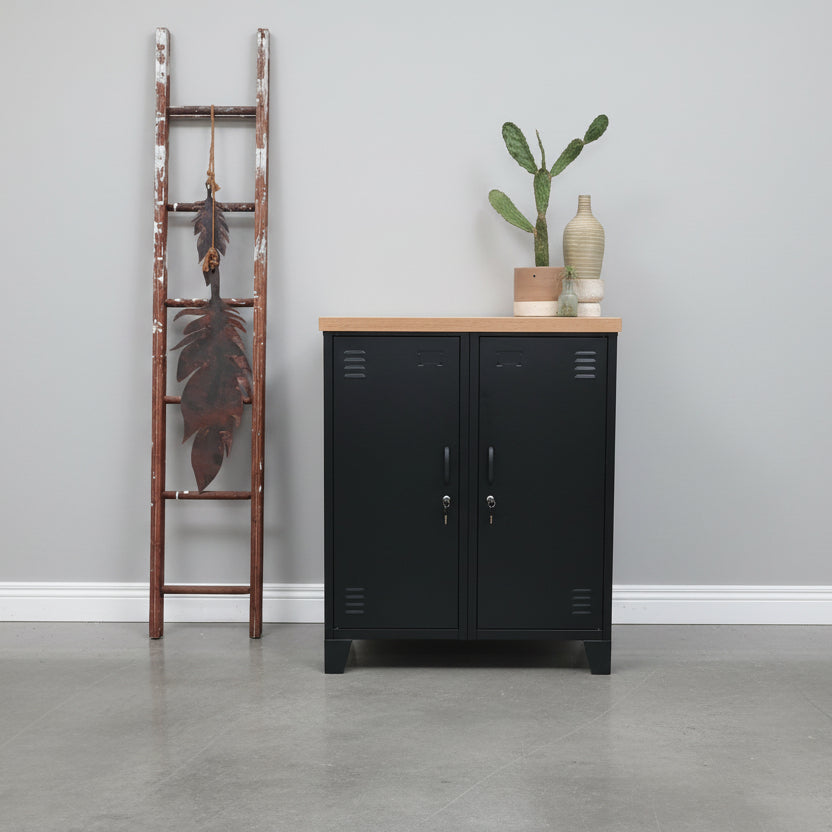 Black metal double side cabinet with oak top against a grey wall with a decorative ladder next to it.