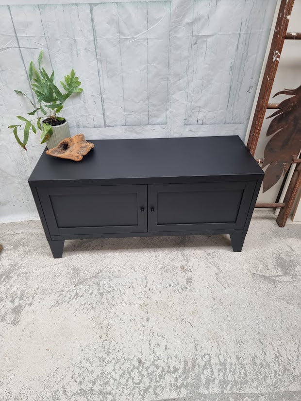 Black metal industrial bench with a plant on a textured floor and light gray wall background