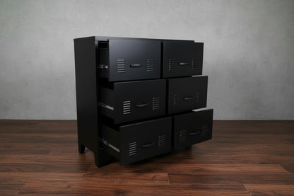 Black metal storage drawer cabinet with multiple drawers against a light gray wall.