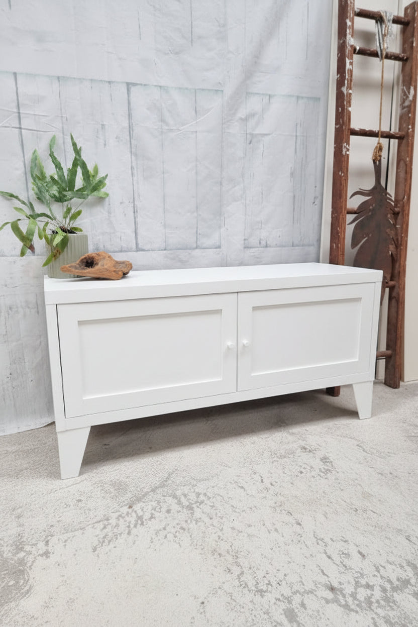 White storage bench with a plant on a gray concrete floor and light gray wall.