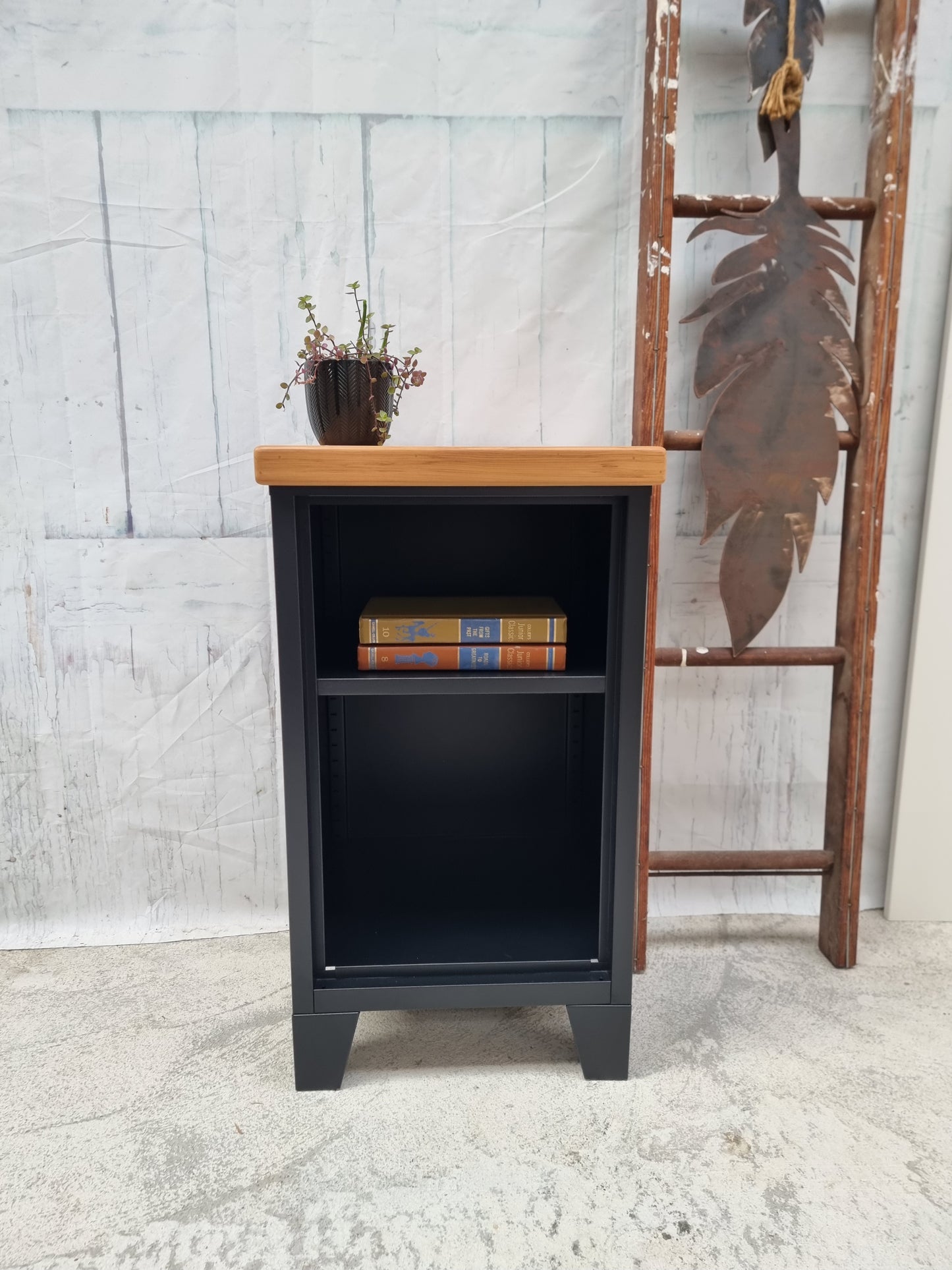 Small black metal industrial bookshelf with a Recycled Rimu top against a textured wall.