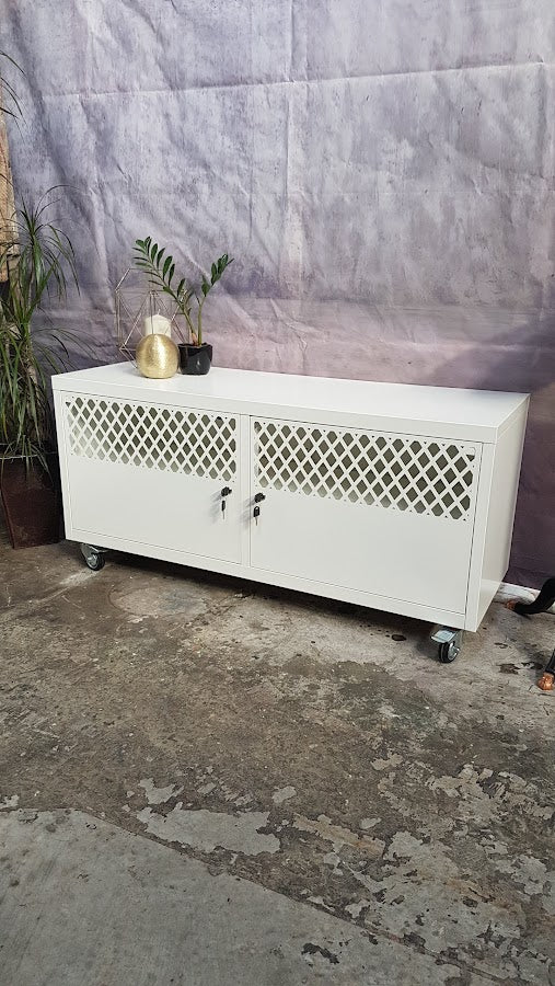 White cabinet with lattice design doors and caster wheels on a concrete floor.