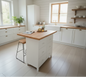 White kitchen island with NZ Recycled Rimu top and 6 drawers in a room with a window and plants.