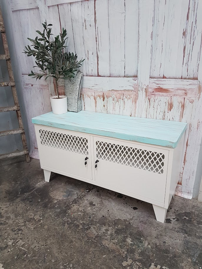 White metal cabinet with lattice design on a light blue countertop against a rustic wooden wall.