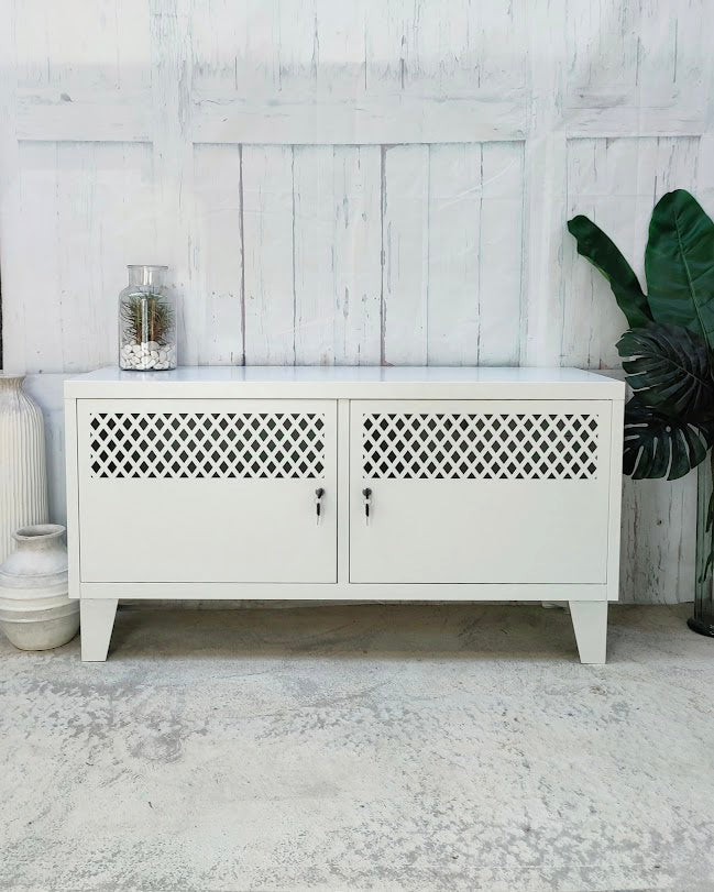 White metal locker cabinet with lattice design doors in a room with a wooden floor and white walls.