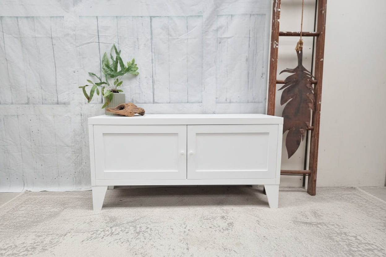 White metal storage bench with a plant on a gray floor against a white wall.