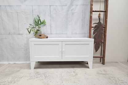White metal storage bench with a plant on a gray floor against a white wall.
