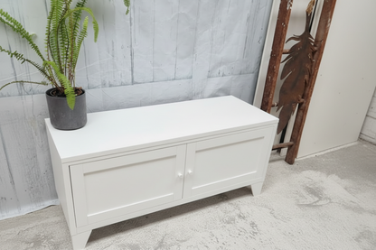 White metal storage bench with a plant on a gray floor against a white wall.