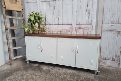 White storage cabinet with wooden top on caster wheels against a rustic wooden wall.