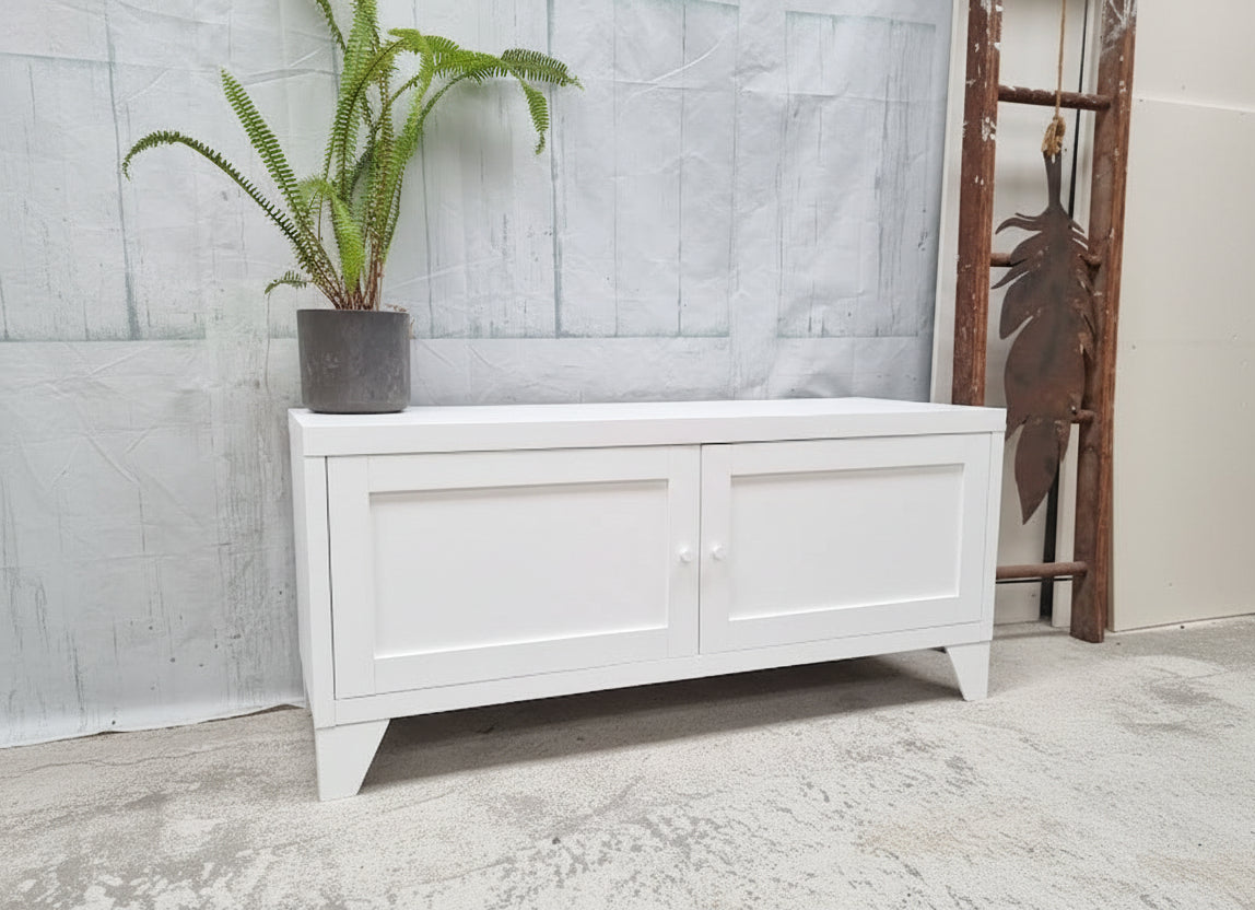 White storage bench with a plant on a gray concrete floor and light gray wall.