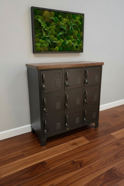 A black 9-door locker with a dark Rimu top, situated against a wall with a moss art above The locker has a industrial style with visible handles and a textured finish.
