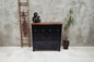 Black metal locker-style dresser with wooden top against a white brick wall.