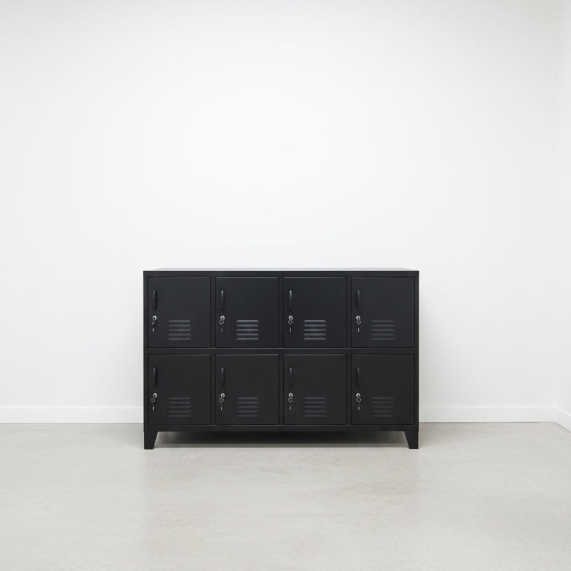 A large black metal locker cabinet with 8 lockable doors stands in a high-ceilinged industrial room.