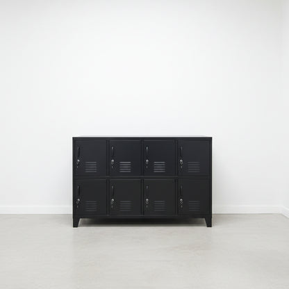 A large black metal locker cabinet with 8 lockable doors stands in a high-ceilinged industrial room.