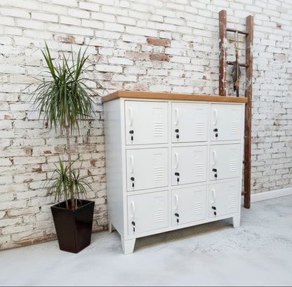 A white 9-door locker with rimu top, featuring white handles and a lock mechanism on each door, positioned against a white background with a potted plant to the side.