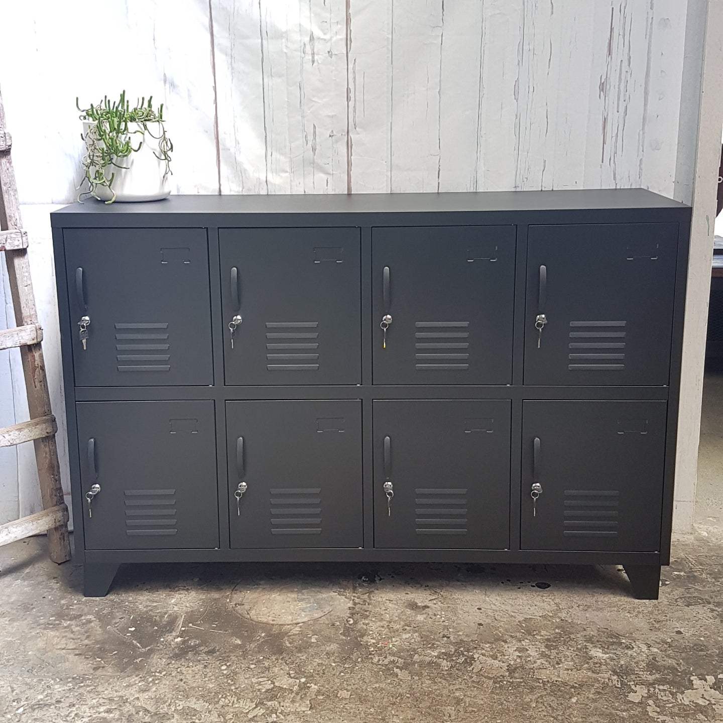 A black metal sideboard locker with eight doors, each with a lock and vent-like design in the center.