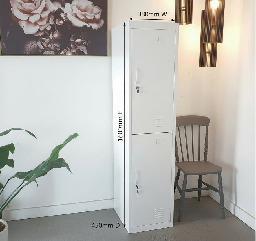 A Slim white 2 door metal locker with a handle, placed in a room with a chair and decorative lighting in the background.