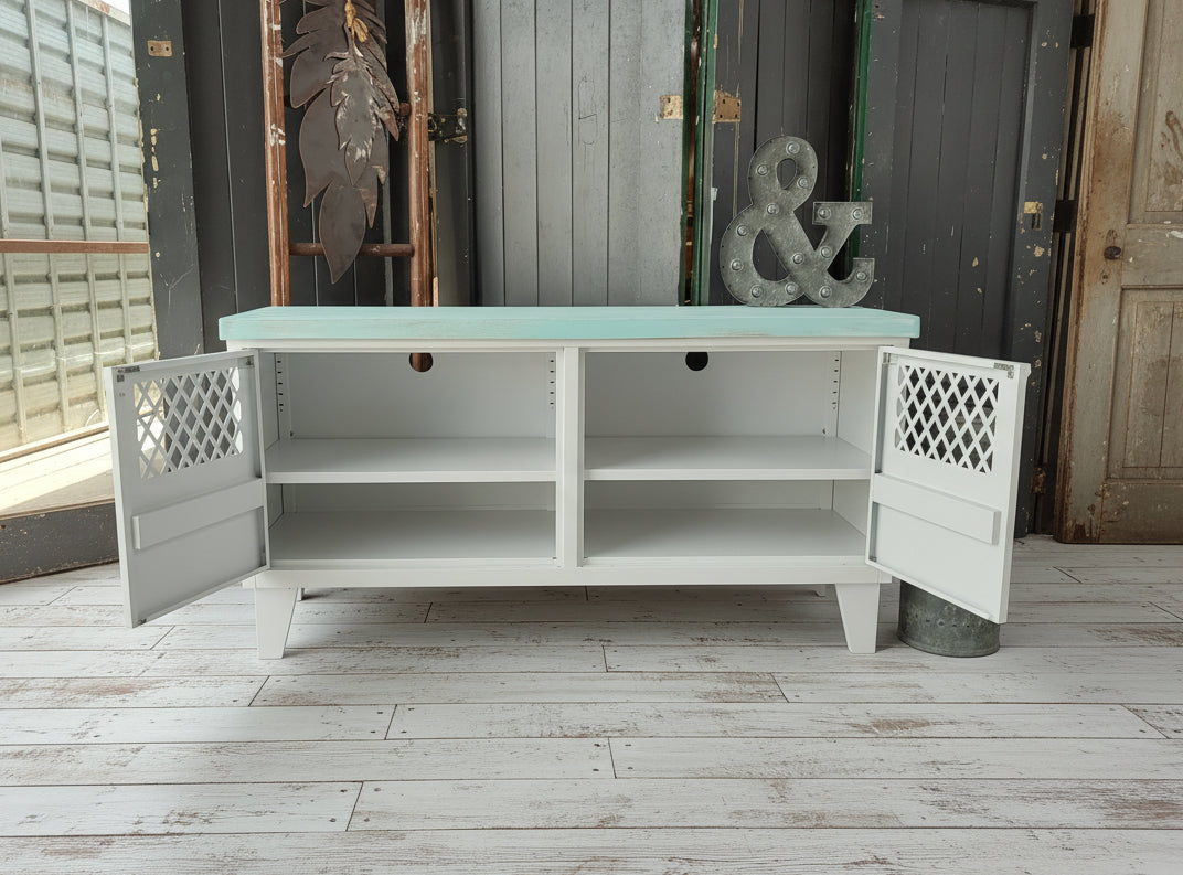 White metal  and wooden console table with open doors showing adjustable shelves and cable holes on a wooden floor.