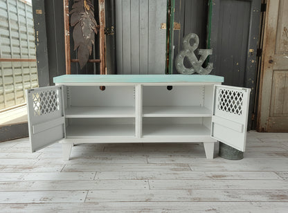 White metal  and wooden console table with open doors showing adjustable shelves and cable holes on a wooden floor.