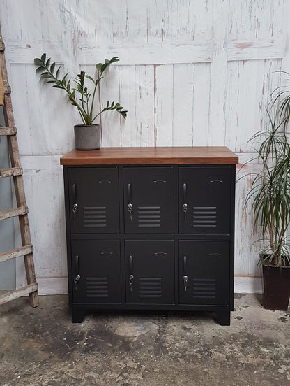 A black 6-door locker with dark oak top, featuring metal grid patterns on the doors, placed against a white background with a plant to the side.