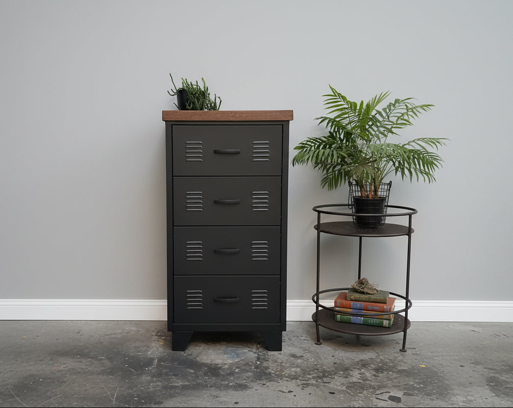 A black metal 4-drawer cabinet with a dark oak top, positioned in a room with a plant and a round metal side table beside it.