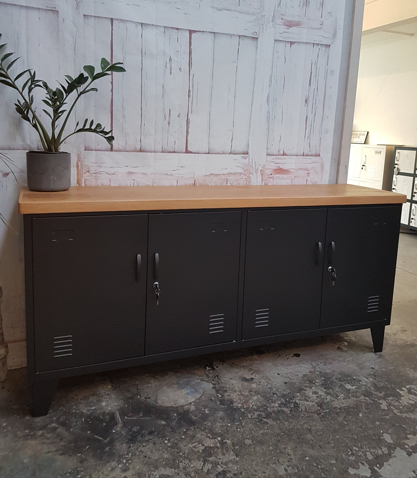 A black versatile metal locker with an oak top, featuring multiple doors and set against a distressed wooden backdrop.
