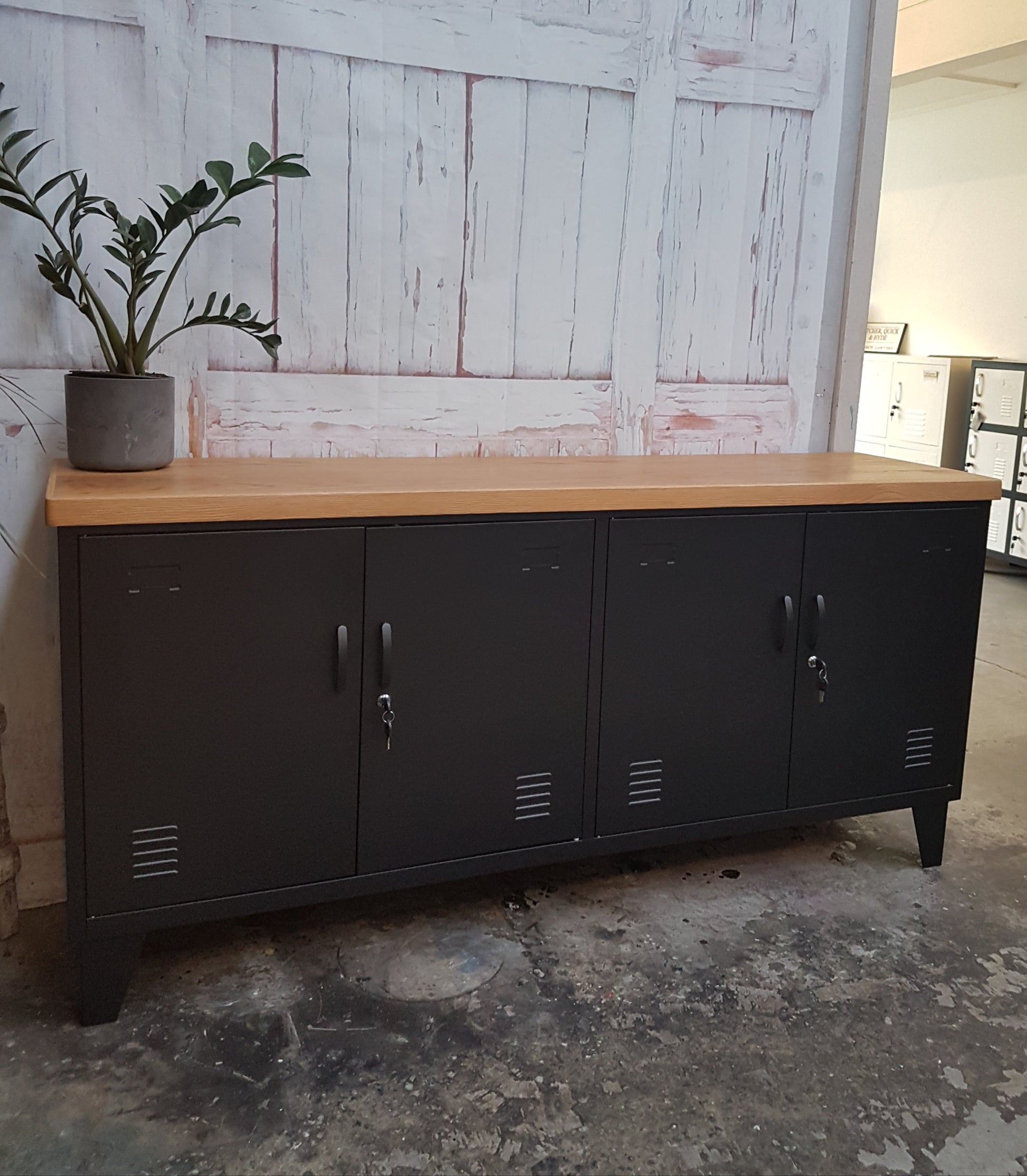 A black versatile metal locker with an oak top, featuring multiple doors and set against a distressed wooden backdrop.