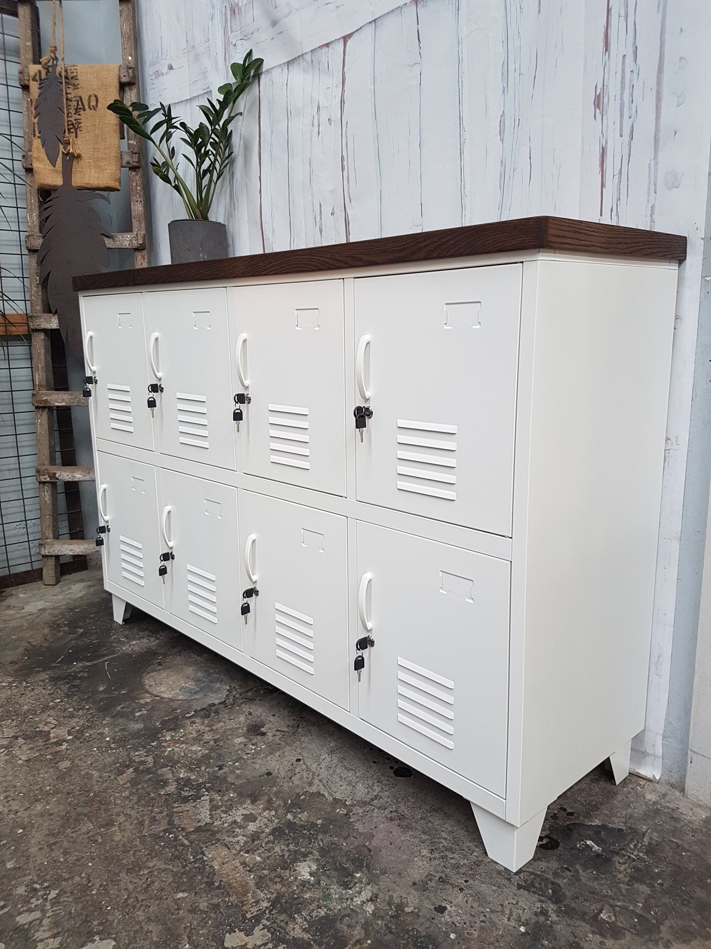 A white 8-door sideboard locker with a Dark oak top, featuring individual lockers and a handle on each door, set against a rustic backdrop