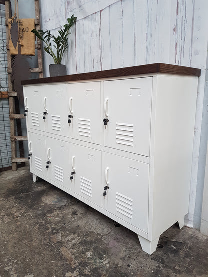 A white 8-door sideboard locker with a Dark oak top, featuring individual lockers and a handle on each door, set against a rustic backdrop